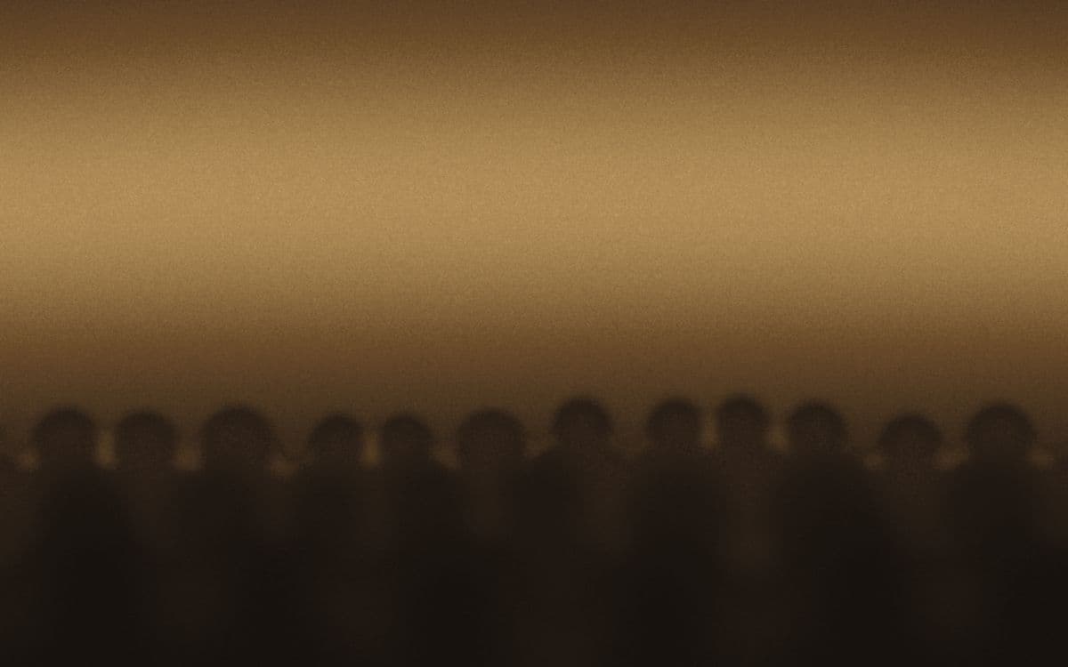 Rows of listeners in a darkened hall, lit only by the light they are facing.
