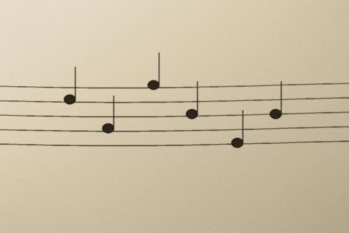 A staff of hand-ruled sheet music with a few noteheads, lit from the side.