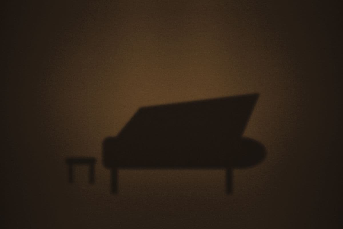 A grand piano with its lid raised, silhouetted in a pool of stage light.