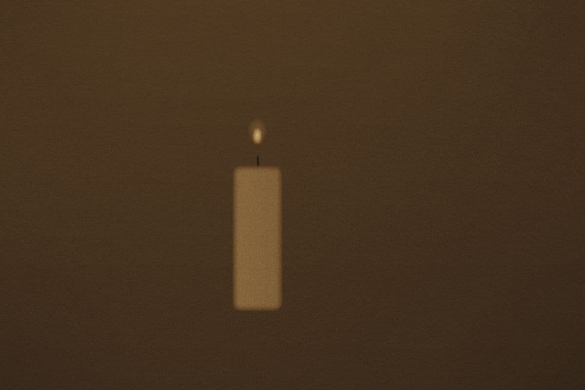 A single lit candle on a dark table, its light pooling on the wood.
