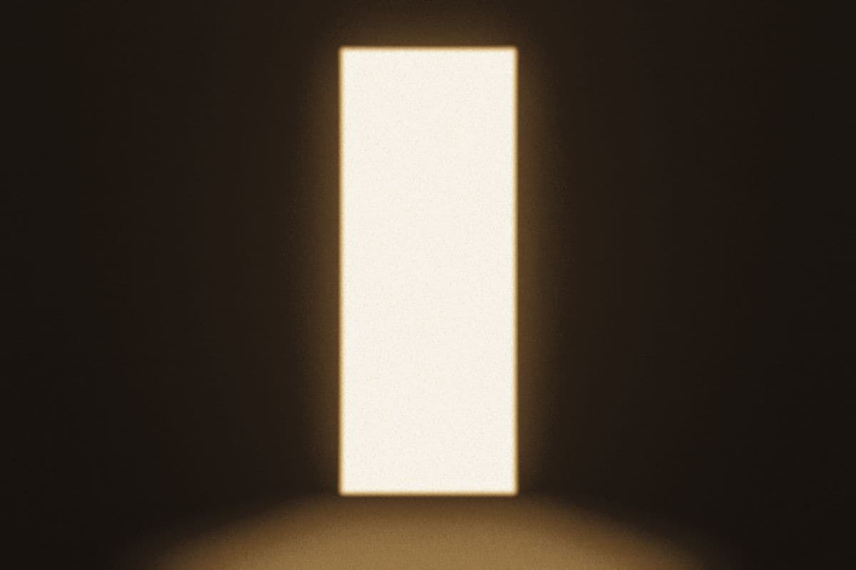 An open doorway filled with warm light in an otherwise dark room.