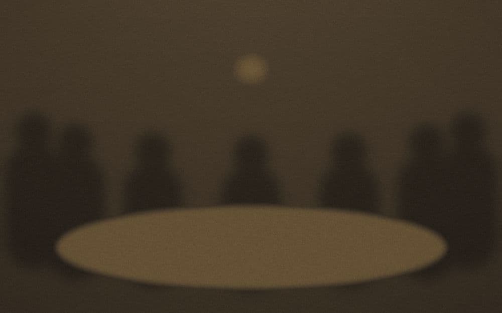 A circle of seated figures around a lamplit table.