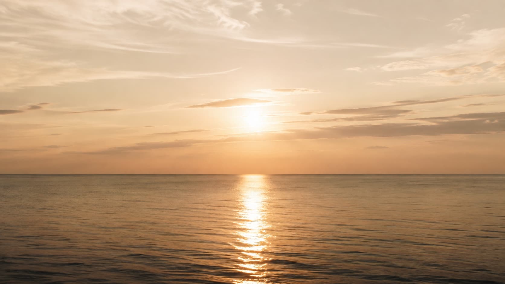 A low horizon at dusk with a path of light reflected across still water.