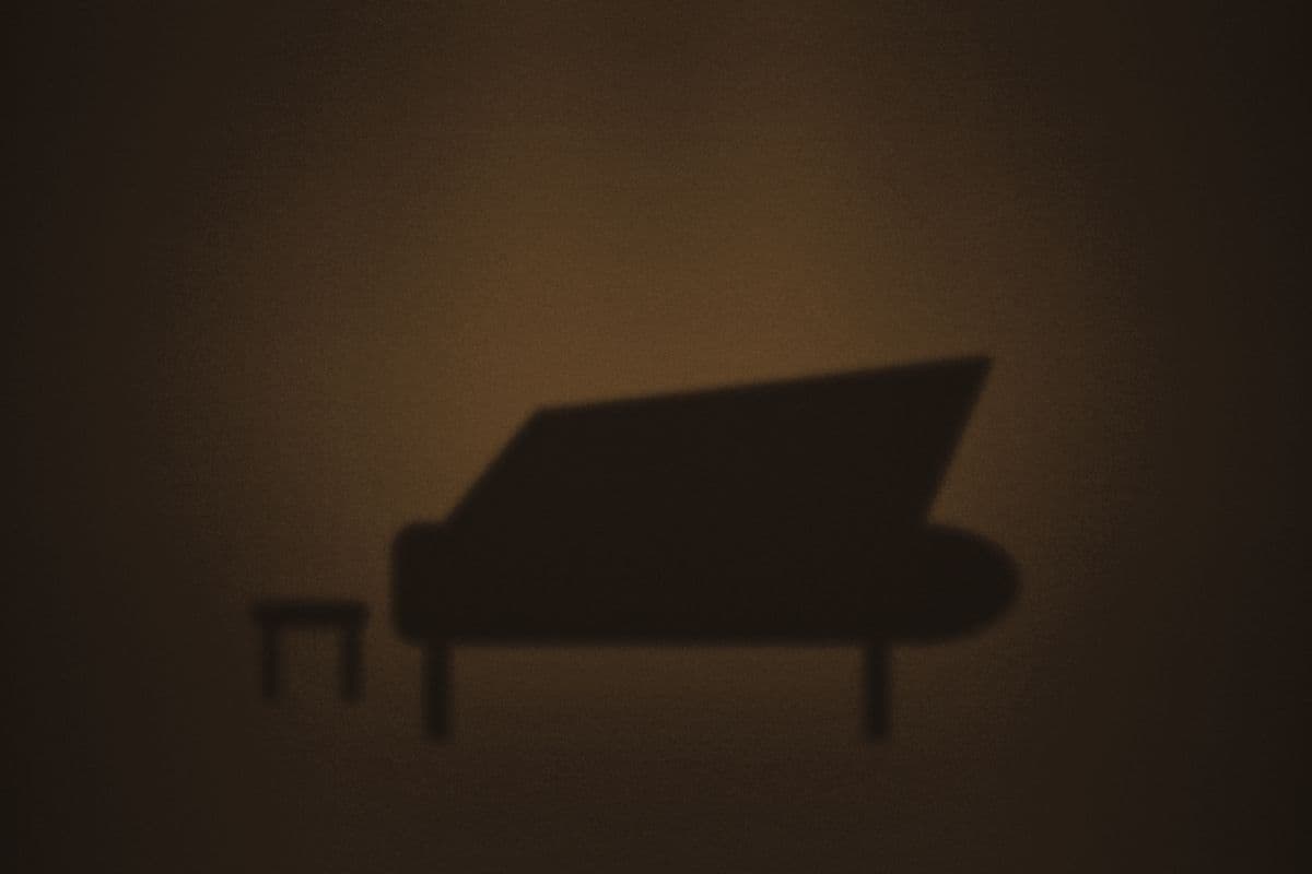 A grand piano silhouetted in a pool of light on a dark stage.